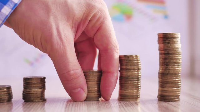 Man hand holding coin dollar on money coin stack arranged as a graph on wooden table. Hand of male or female finger step coins stack growing growth saving money. Business idea.