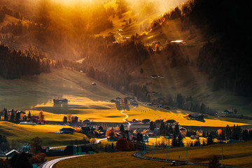 Sun beams lighting through the clouds and falling down to the little village on the hill, vivid colors of sunset, waves of green fields