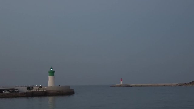 Lighthouse shining on the dawn filmed from a yacht coming out of the port to the sea