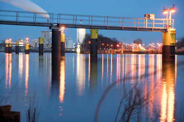 Footbridge in front of Weser weir (Weserwehr) and Weser lock (Weserschleuse), Bremen-Hemelingen, Germany at night with light reflections on water - obrazy, fototapety, plakaty