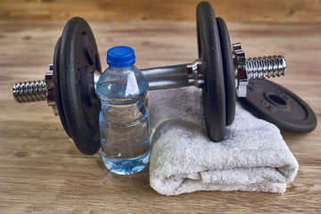 Fitness workout, slimming exercises, weight loss and diet healthy eating concept, dumbbells, bottle of mineral water and towel on wooden floor of training class