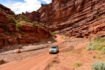 Desert Canyon Road - A 4X4 SUV vehicle is crossing over a spring creek on a dirt-road in a steep canyon (Onion Creek Trail) near Colorado River Scenic Byway (U-128), Moab, Utah, USA. © Sean Xu
