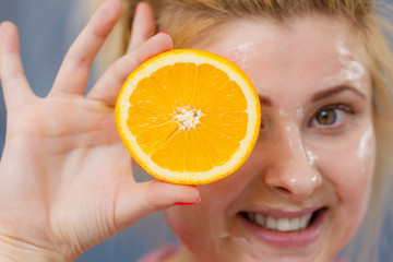 Woman having gel mask on face holding orange