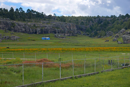 Landschaft in Mexiko in der Nähe von Creel mit hellblauem Farmhaus zwischen Feldern und vor Felsformationen