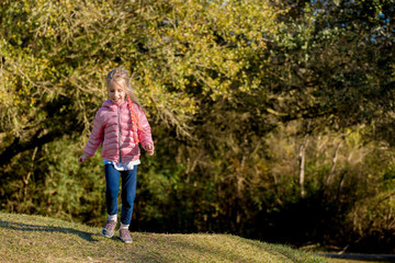 Happy little girl smiling, with ponytail, running on grassy hill in the park