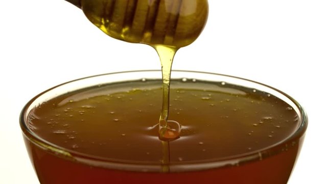 Pouring honey full HD slow motion close-up video isolated on white background. Sweet viscous liquid falling into bowl from wooden dipper - Powered by Adobe