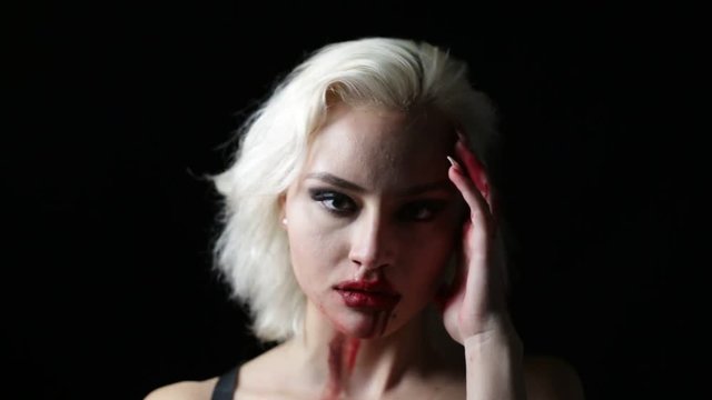 Fashion blonde with bloody hands and face. Young blond woman posing on black with blood on face. Shallow depth of field