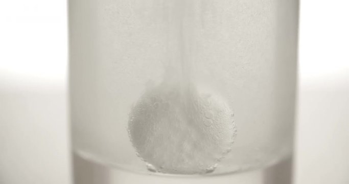 Effervescent aspirin tablet dropping to glass of water 4k video. Extreme close up slow motion fizzy pill falls dissolves with bubbles. Medicine, health care pharmacy chemistry concept