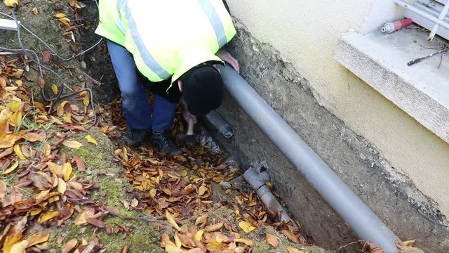 A person carries out plumbing work to replace a water pipe outside the house.
