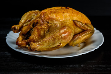 roast chicken on a white plate, on a black wooden background