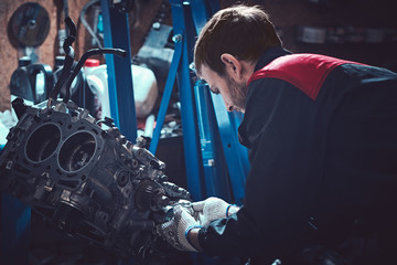 The young auto mechanic dismantles the opposing engine. - obrazy, fototapety, plakaty