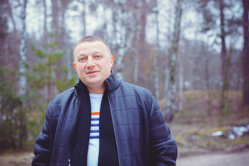 Portrait of a middle age man in warm clothing at forest on a cold day. Fashion handsome elegant man wearing black coat in winter day over trees forest background 