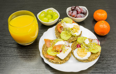 A plate with healthy rye bread sandwiches, fruit and juice for breakfast.