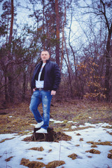 Fototapeta premium Portrait of a middle age man in warm clothing at forest on a cold day. Fashion handsome elegant man wearing black coat in winter day over trees forest background 