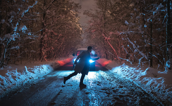 The Man Running On The Snowy Road Against The Car. Evening Night Time