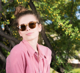 Cute young woman wearing sunglasses outdoors. Pink shirt, hair wrapped