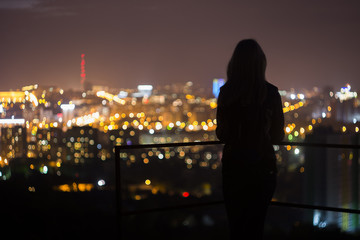 Girl is standing on the roof and looking at the night city