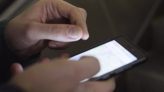 A man is riding an escalator in the subway. Man searches location on map in phone. Close-up.