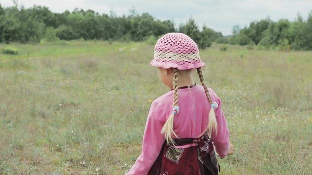 little girl in a pink hat, a pink sweater and red dress running through field with yellow wildflowers in the hands