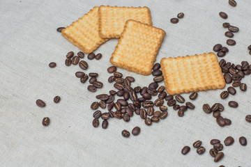 The background of a gray cloth made of old and coarse burlap, on which lies a certain amount of brown coffee beans with a yellow rectangular biscuit