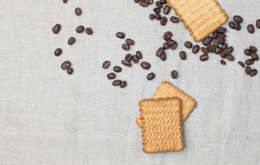 The background of a gray cloth made of old and coarse burlap, on which lies a certain amount of brown coffee beans with a yellow rectangular biscuit