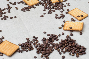 The background of a gray cloth made of old and coarse burlap, on which lies a certain amount of brown coffee beans with a yellow rectangular biscuit