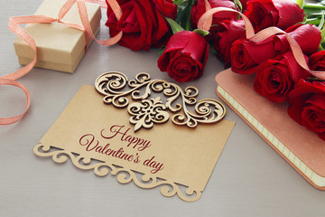 Valentine's day background. Beautiful bouquet of roses next to letter with text HAPPY VALENTINES DAY on wooden table.