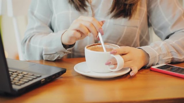 Woman enjoys drink coffee in cafe, mixing sugar