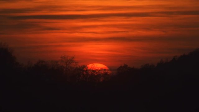 Beautiful sunset with sun setting behind trees on a hill