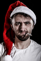 Unshaven man in a Christmas hat smoking a cigarette