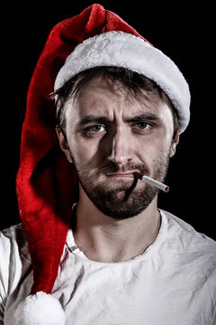 Unshaven man in a Christmas hat smoking a cigarette