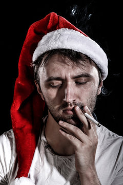Unshaven man in a Christmas hat smoking a cigarette