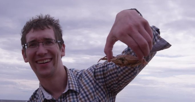 Man holds crab up towards camera while on beach - slow motion close up