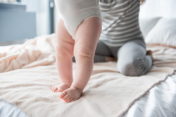 Obraz na płótnie Canvas Close up of infant legs standing on bed, female sitting on background. Focus on feet