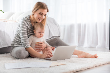Full length of cheerful woman relaxing with little child on the floor and showing her laptop