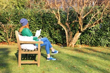 Girl reading a book on a wooden bench in a park. Italy