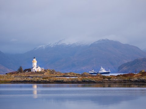 Lighthouse on Isle of Ornsay, the southern side of Isle of Skye, Scotland. Trade ship at rocky island,