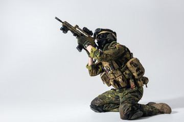 Side view severe soldier shooting with assault rifle while locating on knees. Tactic concept. Copy space