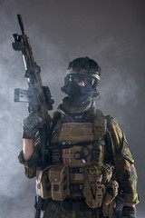 Portrait of serious soldier wearing army clothes while keeping assault rifle in arms. He locating...