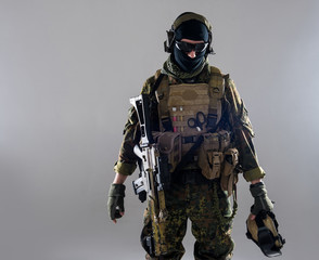 Portrait of calm man wearing balaclava and bulletproof vest while holding helmet and weapon in...