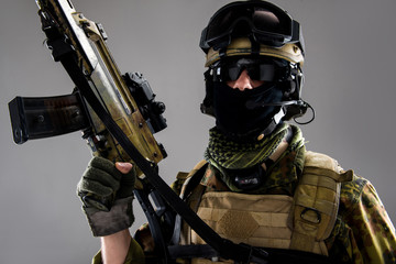 Obraz premium Portrait of severe man wearing helmet, balaclava and special microphone while holding weapon in arm. Military concept