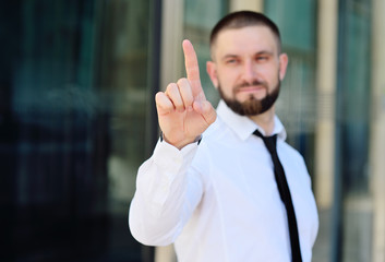 a young man in a white shirt and tie is pressing his index finger on the virtual screen of the touch screen on the background of a glass office building