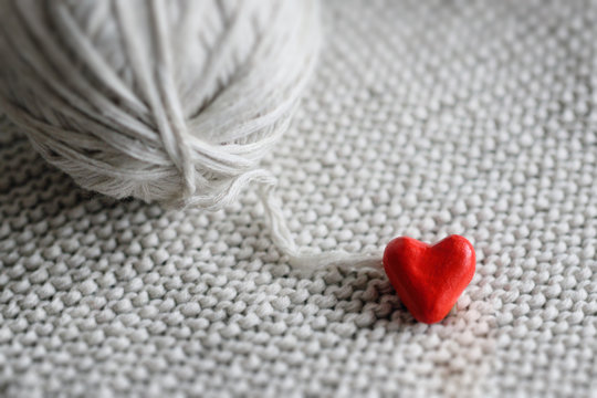 red heart and a ball of threads on a knitted background close-up