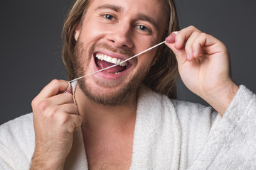 Portrait of content longhaired man using dental floss. Isolated on grey background