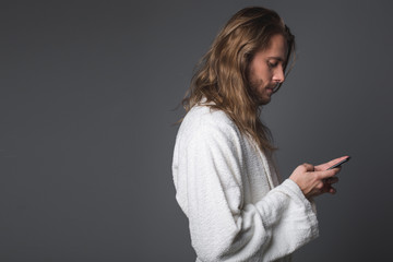 Side view profile of attentive longhaired guy using cellphone. Isolated on grey background. Copy space in left side