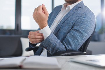 Always good looking. Fashionable clerk sitting on office chair and buttoning on cuff. Close up of his arm