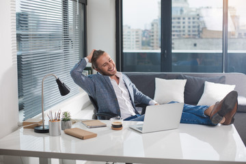 Portrait of fashionable male resting at work. He is smiling broadly and touching his hair