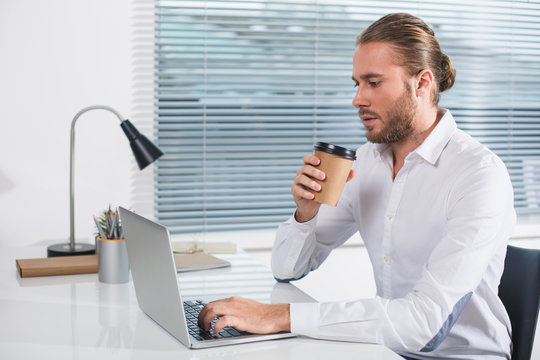Time to relax. Side view profile of intelligent male sitting in the office. He is holding cup of drink and using notebook