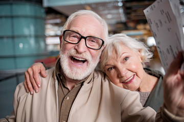 Happy journey. Portrait of delighted old romantic couple is standing at modern terminal. They are...