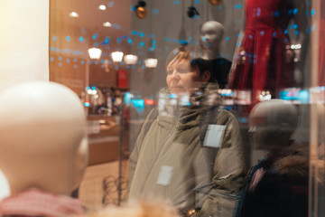 Thoughtful woman looking through shop window at night - obrazy, fototapety, plakaty